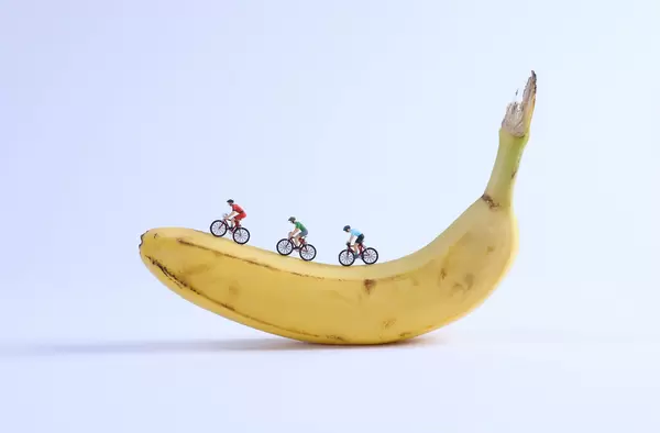 Miniature cyclists on banana on white background