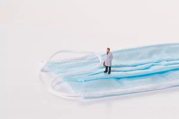 Miniature doctor standing on medical face mask with white background