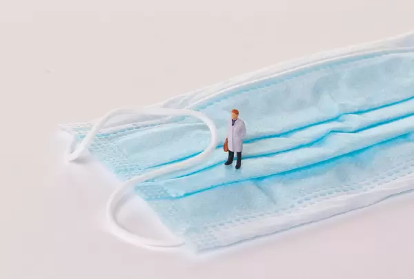 Miniature doctor standing on medical face mask