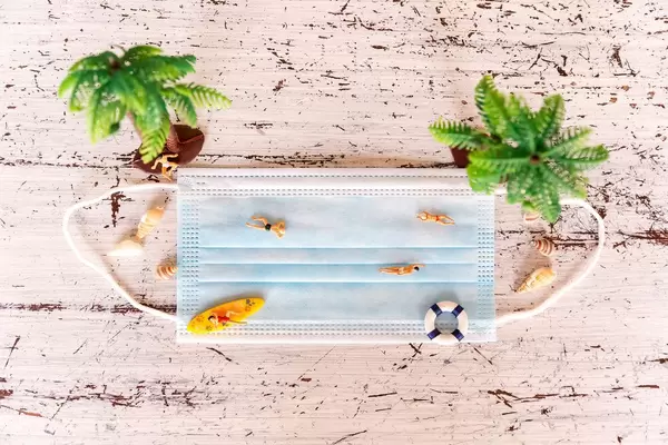 Miniature figures of holiday-makers sunbathing and swimming on a face mask. Summer holidays in 2020