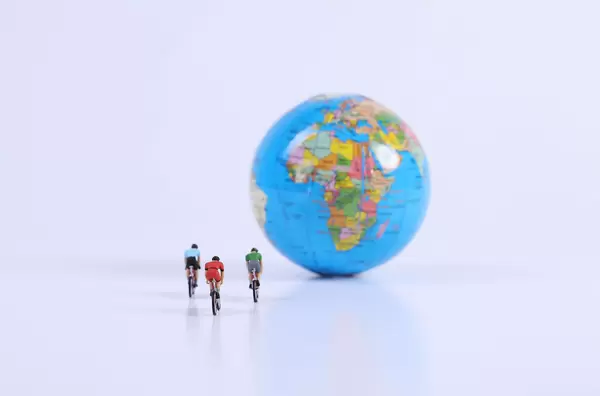 Miniature figures ride bicycle with globe on white background