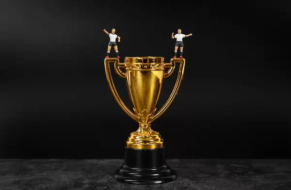Miniature football players standing on golden trophy