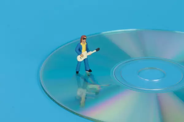 Miniature guitar player standing on CD