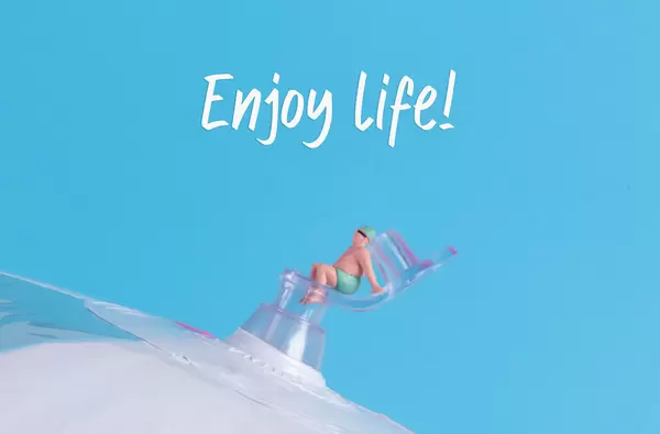 Miniature man in swimsuit sitting on a beach ball with Enjoy Life text