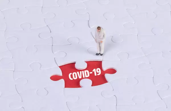 Miniature man looking at a missing puzzle piece with Covid-19 text