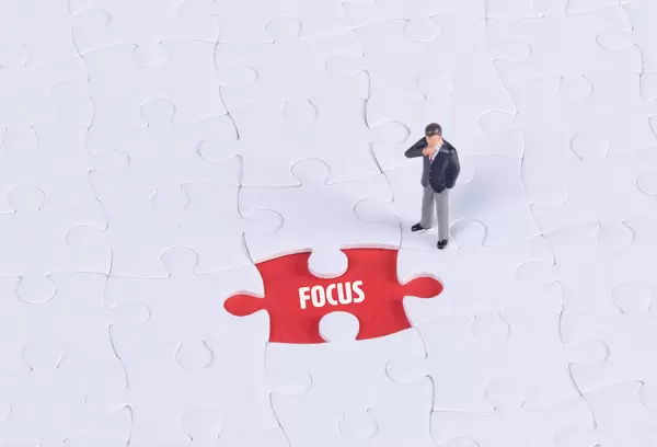 Miniature man looking at a missing puzzle piece with Focus text
