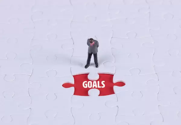 Miniature man looking at a missing puzzle piece with Goals text