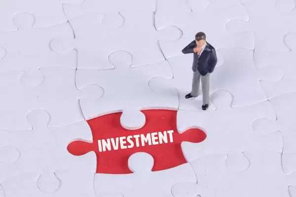 Miniature man looking at a missing puzzle piece with Investment text
