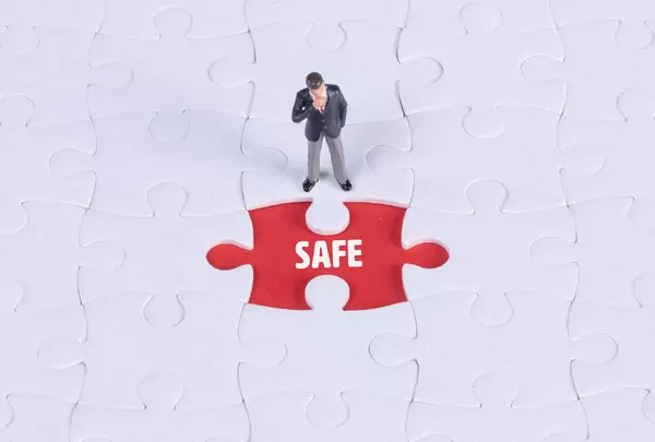 Miniature man looking at a missing puzzle piece with Safe text