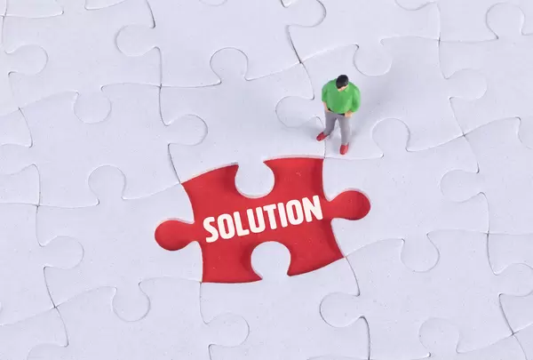 Miniature man looking at a missing puzzle piece with Solution text