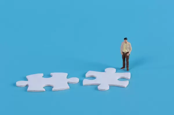 Miniature man looking at two jigsaw puzzle pieces