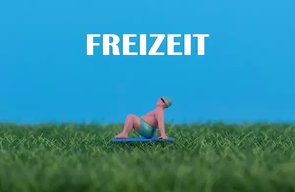 Miniature man relaxing on green grass with Freizeit text