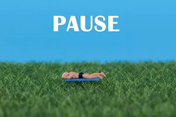 Miniature man relaxing on green grass with Pause text