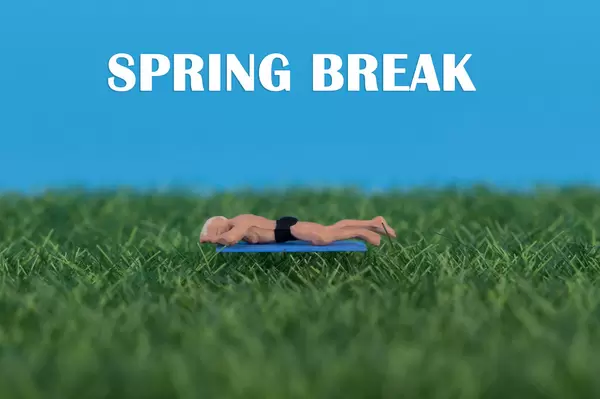 Miniature man relaxing on green grass with Spring Break text