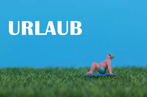 Miniature man relaxing on green grass with Urlaub text