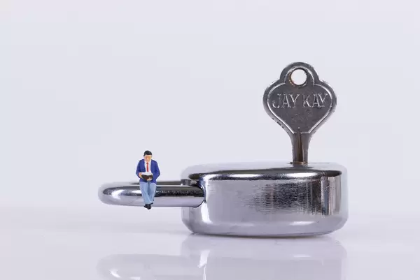 Miniature man sitting on a padlock