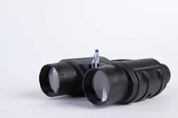 Miniature man sitting on binoculars