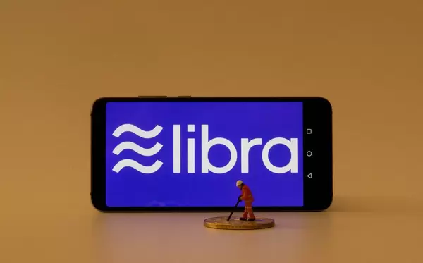 Miniature mining worker next to smartphone with Libra logo