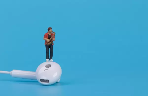 Miniature musician with earbud on blue background