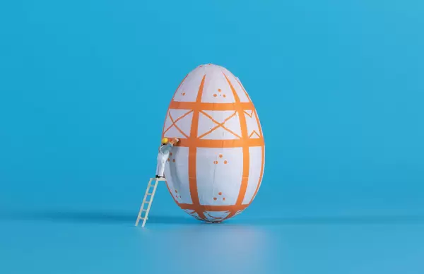 Miniature painter painting easter egg on blue background