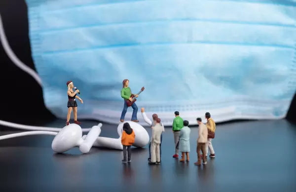 Miniature people at the concert with face mask in the background