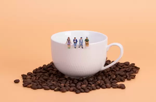 Miniature people: business team sitting on cup of coffee with morning news. Coffee time of business concept.