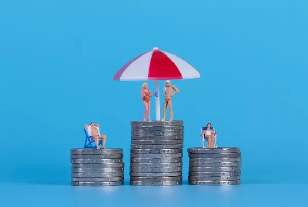 Miniature people in swimsuit on a top of coinstacks with blue background