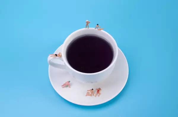 Miniature people relaxing around the coffee cup on blue background