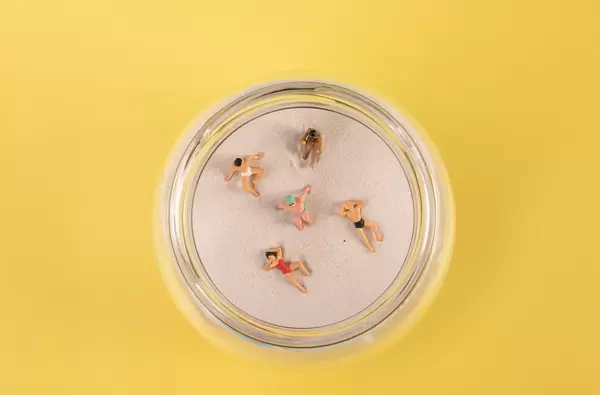 Miniature people relaxing on the sand in glass jar on yellow backgorund