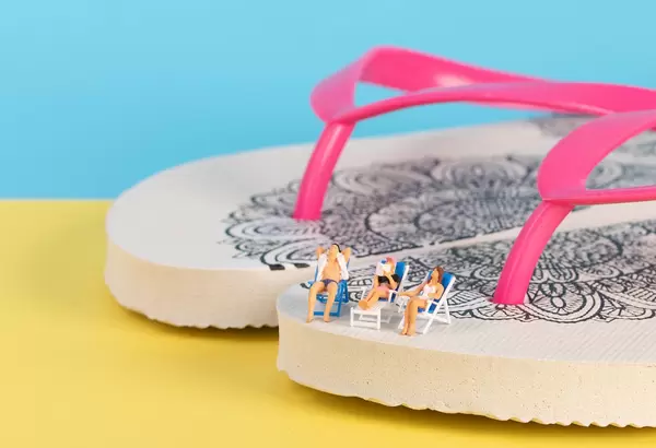 Miniature people sitting in deck chairs on top of the flip flops