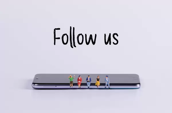 Miniature people sitting on smartphone with Follow us text