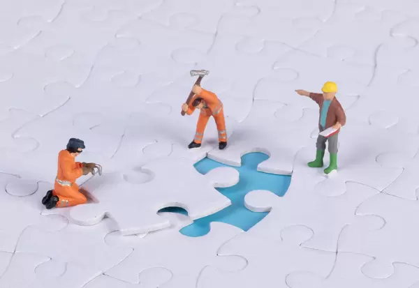 Miniature people team trying to complete the last jigsaw puzzle piece. Teamwork concept