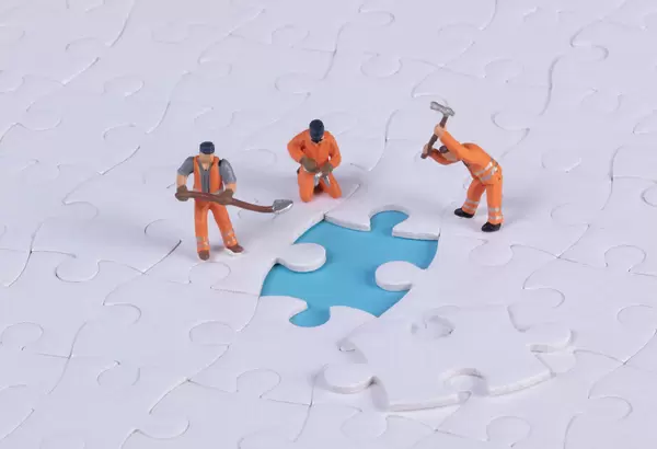 Miniature people team trying to complete the last jigsaw puzzle piece