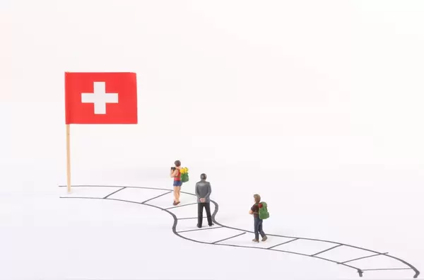 Miniature people walking on a path to the flag of Switzerland