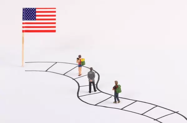 Miniature people walking on a path to the flag of USA