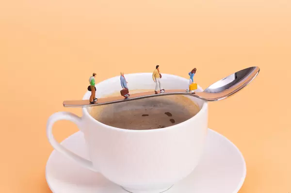 Miniature people walking on the spoon over the hot cup of coffee