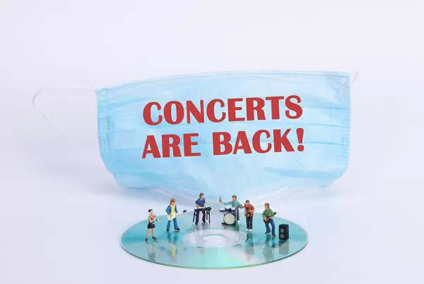 Miniature rock band standing on CD and medical face mask with Concerts are back text