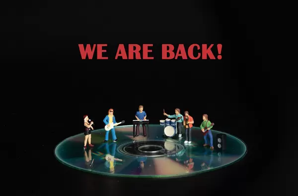 Miniature rock band standing on CD and We are back text
