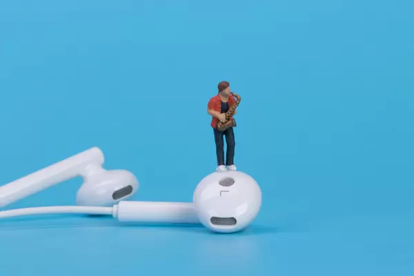 Miniature saxofonist with earbuds on blue background
