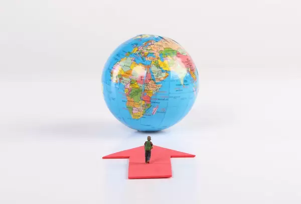 Miniature traveler with red arrow and globe on white background