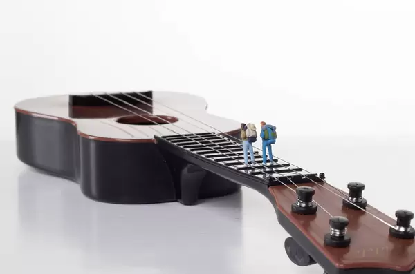 Miniature travelers on a guitar with white background