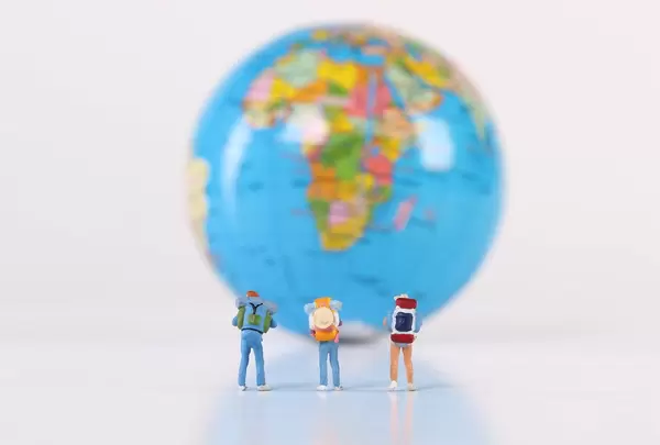 Miniature travelers stading in front of globe