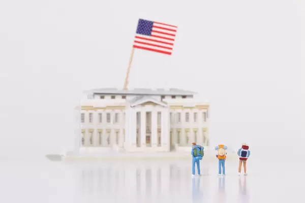 Miniature travelers stading in front of the White House on white background