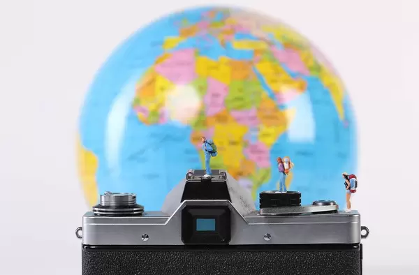 Miniature travelers standing on camera with globe in the background