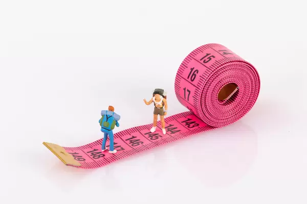 Miniature travelers standing on measure tape