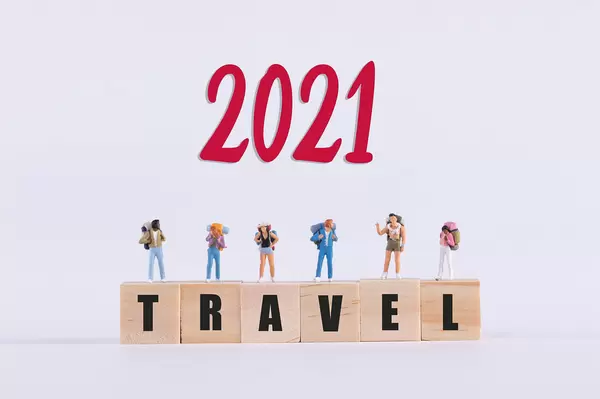 Miniature travelers standing on wooden cubes with Travel text and red 2021 text