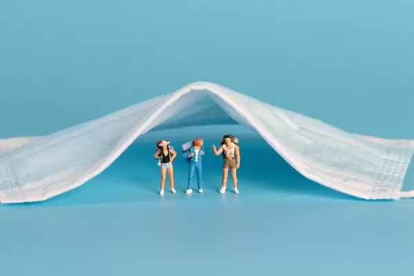 Miniature travelers standing under medical face mask
