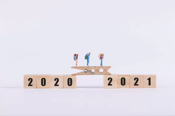 Miniature travelers walking on wooden bridge between 2020 and 2021 text