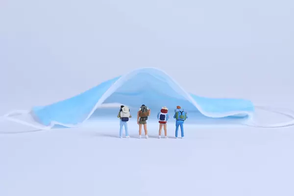 Miniature travelers with medical face mask on blue background