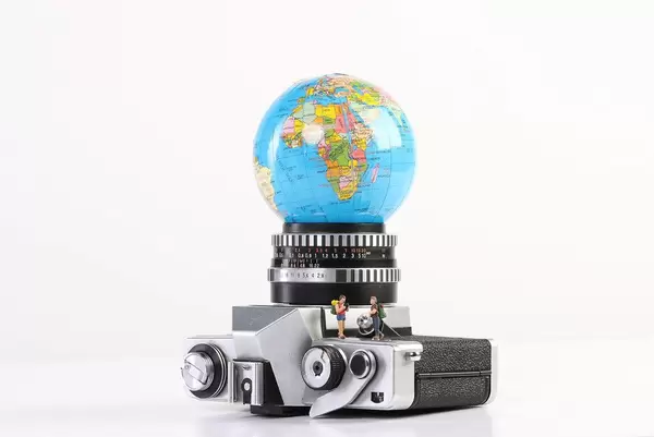Miniature travelers with vintage camera and globe on white background